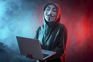 Digital Information Protection Prints: Hacker with anonymous mask with a computer and with a background of smoke and colored led