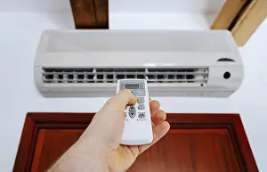Hand Holding Remote Control Prints: Hand holding remote control in front of the air conditioner