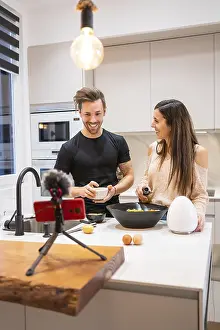 Happy Couple In The Kitchen Prints: Horizontal photo with copy space of a couple cooking and using mobile phone for streaming tutorial