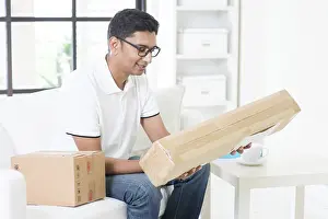 Handsome Indian Guy Looking At Camera Prints: Indian guy received an express parcel and checking the box at home