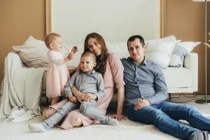 Studio Shot Diversity Prints: Junge gluckliche Eltern, die mit kleinen Kindern auf dem Boden sitzen und in die Kamera schauen Junge gl
