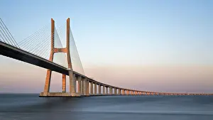 Portugal Tourist Attraction Prints: A long cable-stayed bridge spans over water under a gradient sunset sky