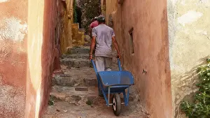 Greek Tourist Attractions Prints: A man pulls a wheelbarrow up a narrow