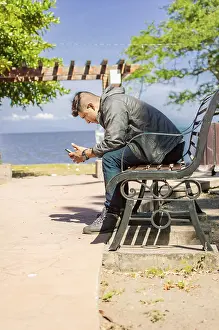 Man Checking Phone Prints: Man sitting on a bench checking his phone