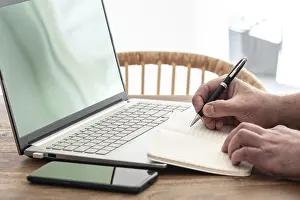 Man Working From Home Prints: man taking notes on paper while using laptop computer