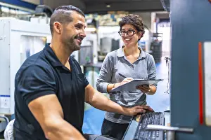 Industrial Building Design Prints: Manager and worker talking while working using computer in a cnc metal factory