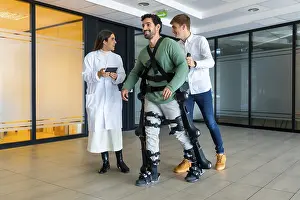 Young Adults With Disability Prints: Mechanical exoskeleton, female doctor with device walking with disabled person with robotic skeleton in rehabilitation
