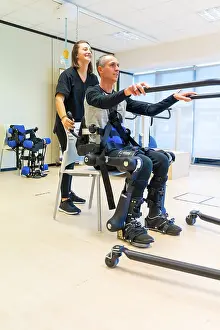 Mechanical Exoskeleton Prints: Mechanical exoskeleton. Female physiotherapy doctor assistant lifting disabled person with robotic skeleton to get up