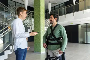 Mechanical Exoskeleton Prints: Mechanical exoskeleton, physiotherapist looking at consultation with tablet with disabled person with robotic skeleton