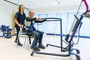 Mechanical Exoskeleton Prints: Mechanical exoskeleton. Female physiotherapy doctor assistant lifting disabled person with robotic skeleton to get up