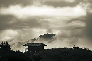 Female Hiker Prints: Mountain hut with bench and climber and dramatic clouds in the background