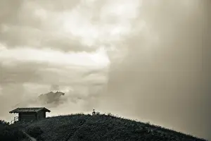 Dramatic Clouds Prints: Mountain hut with bench and climber and dramatic clouds in the background