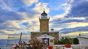 Evening Sun In Greece Prints: An old lighthouse overlooked by a dramatic sky at sunset