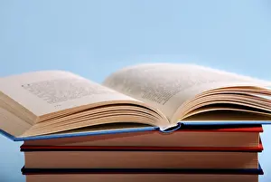 Plain Colored Background Photo Prints: An open book on top of a stack of books against a light blue background