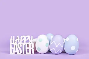 Christian Holiday Decoration Prints: Pastel colored easter eggs and text Happy Easter on violet background with copy space