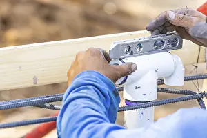 Construction Site Work Prints: Plumber using level while installing PVC pipe at construction site