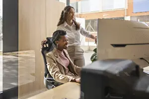 Office Teamwork Prints: Two professionals are engaged at a computer in a bright office