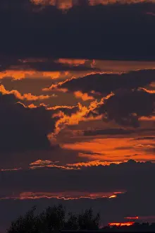 Central Europe Cloudy Skies Prints: Red sun behind clouds in the evening sky