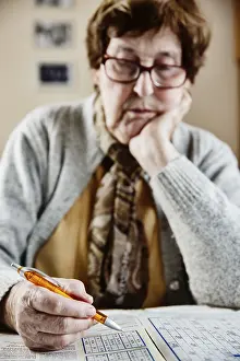 Leisure Activities For Adults Prints: Senior sits at the table at home and solves puzzles