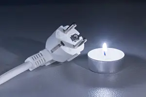 Dark Background Concept Prints: A single candle next to an electrical plug on a dark background