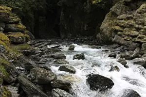 Eroded Canyon Scenery Prints: Small waterfall flows out of a dark cave