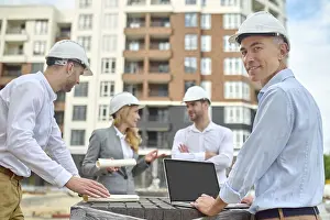 One Person At Work Prints: Smiling contented middle-aged engineer posing for the camera with his colleagues on the background