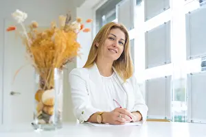 Middle Aged Woman Prints: Smiling estate agent taking notes while looking at camera working in the office