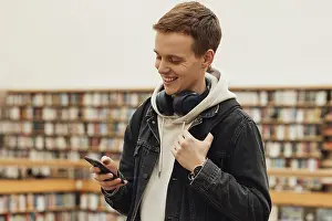 Healthcare System Infrastructure Prints: Smiling student using smartphone while standing in library