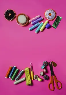 Rainbow Colored Threads Prints: Several spools with cotton threads placed with scissors and set of needles on pink surface