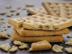Appetizing Baked Goods Prints: Stack of square crackers with pieces and crumbs on slate gray background