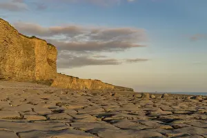 Welsh Coastline Prints: The stones and cliffs of Llantwit Major Beach in the evening sun with some clouds over the cliffs