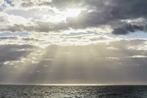 Cloudy Day Europe Prints: Sun breaks through the clouds with sunrays over sea