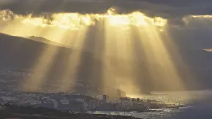 Canary Islands Scenery Prints: Sun rays break through dramatic clouds over a coastal town