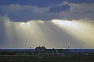 Scottish Coastal Landscape Prints: Sunbeams break through dramatic clouds over houses by the sea