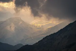 Weather Forecast Images Prints: Sunlight pierces through dramatic storm clouds over a mountain landscape