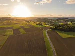 Dramatic Evening Sky Prints: Sunset over sweeping fields with a winding road and dramatic sky