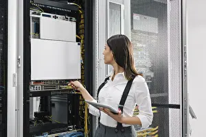 Data Center Professional Prints: Technician using tablet pc while analysing server in large data center