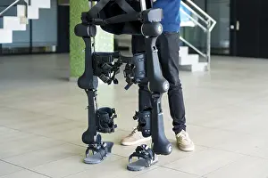 Modern Hospital Equipment Prints: Unrecognizable computer engineer in mechanical exoskeleton looking at the robot with a tablet
