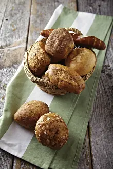 Freshly Baked Goods Prints: Various types of bread in a basket lying on a rustic table