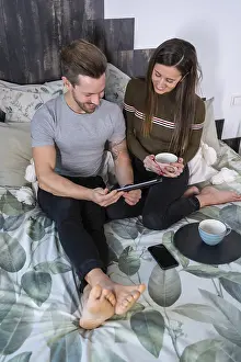 Couple On Bed Prints: Vertical top view of a couple drinking coffee and using tablet on the bed