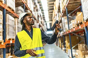 Supply Chain Management Prints: Side view of an african worker scanning package with bar code reader in a distribution warehouse