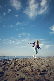 Prints of A woman in casual attire joyfully standing on rocks near the ocean under a sunny blue sky with scattered clouds, Belarus, Minsk Belarus Prints: Belarus Ocean Landscape Print