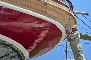 Water Sports Greece Prints: A worker is working on the red hull of a sailing ship