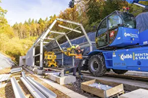 German Railway Infrastructure Prints: Workers use cranes to build a structure along a rail line in the forest