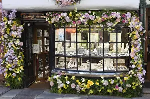 Prints of York in England: Jewelry shop window display framed by colorful flowers with various pieces of jewelry inside, creating an inviting retail scene York Prints: York in England: Colorful Jewelry Shop Print