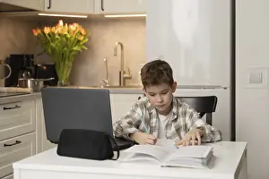 Young Boy Studying Prints: A young boy diligently studies at a table in a cozy kitchen setting