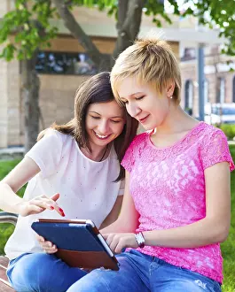 Educational Institution Settings Prints: Young college students using tablet computer while doing homework in the park