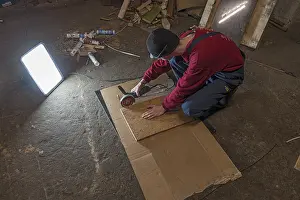 Evening Sky Atmosphere Prints: Young man working with an angle grinder in his workshop in the evening